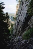 A steep rock wall, a place for training climbers, a secluded area in the forest, a gray stone, a sloping mountain, a granite rock stone. photo