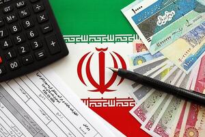 Iranian annual income tax return form F20-25-006 ready to fill on table with pen, calculator and iranian money on flag photo