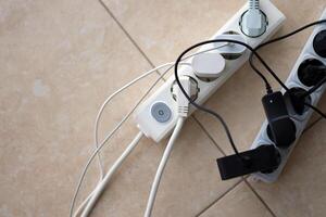 Overloaded power boards. Power strips with different electrical plugs on white floor photo