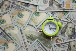 Alarm clock on hundred dollar bills banknotes. Background of time management, business photo