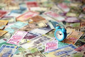 Small alarm clock on many banknotes of different currency. Background of time and money photo