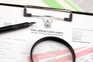 Thailand Visa application form on A4 tablet lies on office table with pen and magnifying glass photo