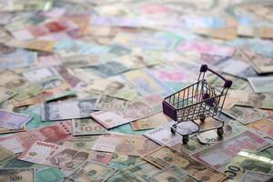 Supermarket trolley on many banknotes of different currency. Background of shopping worldwide photo