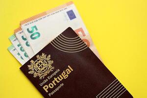 Red Portugal passport of European Union and money on yellow background close up photo