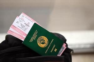 Green Nigerian passport with airline tickets on touristic backpack photo