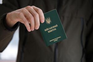 Young ukrainian conscript soldier shows his military token or army ID ticket indoors photo