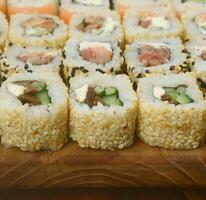 el primer plano de muchos rollos de sushi con diferentes rellenos se encuentra sobre una superficie de madera. foto macro de comida japonesa clásica cocinada con un espacio de copia