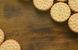 A round sandwich cookie with coconut filling lies in large quantities on a brown wooden surface. Photo of edible treats on a wooden background with copy space