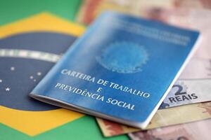 Brazilian work card and social security blue book and reais money bills on flag of Federative Republic of Brazil photo