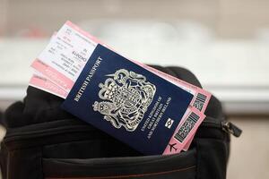 Blue British passport with airline tickets on touristic backpack photo