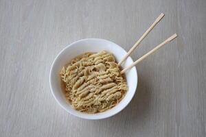 Bowl of instant cooking noodles with wooden chopsticks on white wooden table photo