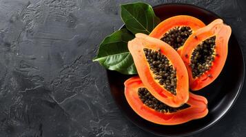 Halved ripe papaya with seeds on a black plate displaying tropical freshness and organic appeal photo