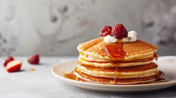 Stack of pancakes dripping with syrup and topped with raspberries and cream for a sweet breakfast treat photo