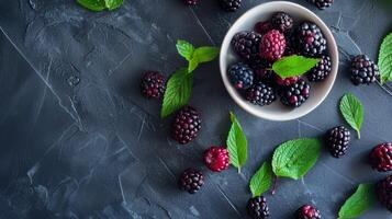 Fresh blackberries and mint leaves in a bowl on dark slate background photo