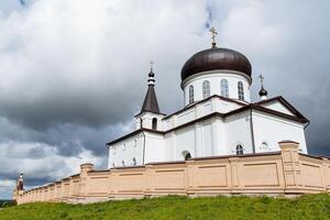 A white brick building is a church church church, a monastery stands behind a brick wall, an Orthodox shrine, a place for repentance, a prayer in the temple. photo