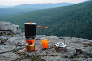 Tourist utensils stand on the edge of a cliff in the mountains, a climber's food, a kitchen in nature, a gas burner, a pot for food, a kettle with water, a hike in the mountains. photo