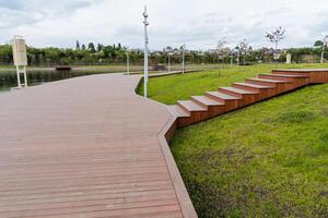 A modern city park, a river embankment, a pedestrian road made of boards, wooden flooring, stairs up, the design of the park is stylish, the concept of outdoor recreation. photo