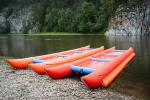 Inflatable catamarans are moored to the shore, red boats of bright color stand on the bank of the river, a boat for boat trips along mountain rivers, tourist equipment. photo