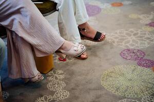 De las mujeres pies en Zapatos sandalias, pedicure en el clavos, muchachas sentar lanzamiento un pie en el pie, señoras' zapatos, verano zapatos, un de colores alfombra. foto