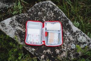 First aid kit in the open form lies on a stone, a first-aid kit in emergency cases, an elastic bandage, tablets in assembly, a set of medicines, a hike. photo
