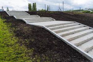 A concrete staircase rises up the hill, a pedestrian path in the park steps descend from above, the improvement of the territory of the city arch for people to relax. photo