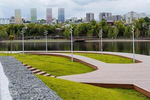 Park in the center of the city on the pond, the city modern recreation park, wooden walking paths, landscape design, no people, lake promenade panorama. photo