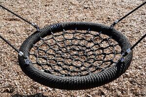 Children's swings hang on the background of the ground, a braided round cloth, a web of nylon harness, a black rope. photo