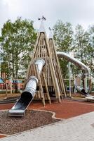 un grande Deportes jugar complejo para niños en el abierto aire, un para niños patio de recreo hecho de madera en el ciudad parque, un metal deslizar, un pirámide de registros, un atracción para niños. foto