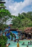 Jepara, Central Java, April 14, 2024 - Swimming pool rides surrounded by trees are full of visitors during holidays. photo