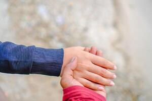 the hands of a couple holding hands against the background of beach sand. photo