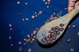 Black coffee beans are seen close up with a wooden spoon on a black cloth. photo