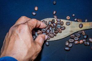 Black coffee beans are seen close up with a wooden spoon on a black cloth. photo