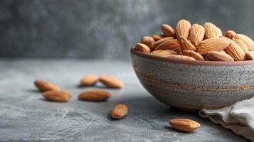 Almonds in a ceramic bowl on a textured grey background showcasing healthy, snack, food, organic, nutrition, and vegetarian elements photo