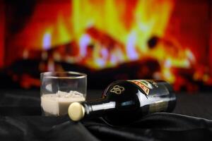 KYIV, UKRAINE - MAY 4, 2022 Baileys original alcohol bottle on wooden table with red fireplace photo