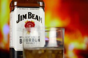 KYIV, UKRAINE - MAY 4, 2022 Jim Beam original alcohol bottle on wooden table with red fireplace photo