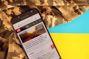 KYIV, UKRAINE - 4 MAY, 2023 NV ukrainian news portal on smartphone screen with ukrainian flag and camouflage fabric photo