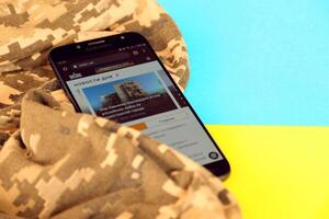 KYIV, UKRAINE - 4 MAY, 2023 Unian ukrainian news portal on smartphone screen with ukrainian flag and camouflage fabric photo