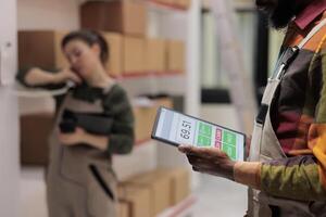 Warehouse supervisor holding tablet computer analyzing checklist, preparing clients order. Diverse employees working at packages delivery, scanning products in storage room. Close up concept photo