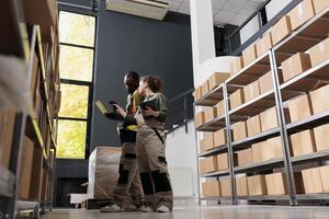 Diverse stockroom team looking at cardboard boxes, working at merchandise inventory in storehouse. African american supervisor and manager preparing customers orders for delivery in storehouse photo