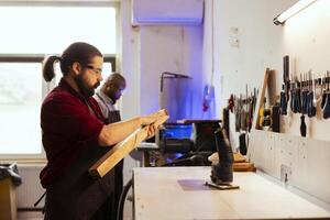 Carpenter wearing protection glasses, checking for scratches on wood before assembling furniture. Cabinetmaker using safety equipment in joinery, running hand along lumber block, running evaluation photo