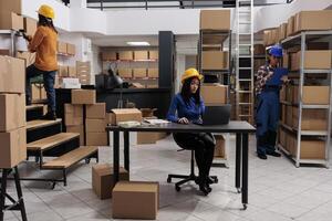 Asian delivery service employees team working in warehouse together. Storehouse workers tracking parchel shipment on laptop, searching parcel on rack and doing inventory management photo