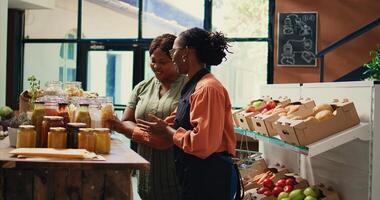 Merchant presenting homemade sauces and spices to client, promoting local farming and healthy eating. Storekeeper recommending bio organic bulk products at supermarket. Handheld shot. photo