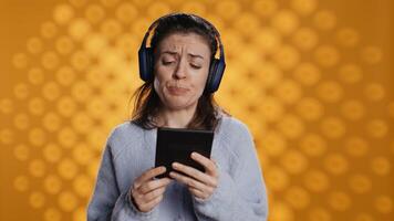 Voice actor frowns while reading ebook, portraying character, studio background. Woman reenacting digital recording of novel, interpreting furious antagonist, reading text from tablet, camera B photo