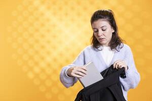 Portrait of woman rummaging through backpack, taking book out, isolated over studio background. Student removing textbook used for educational purposes from school rucksack photo