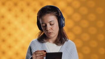 Woman reading ebook on ereader and listening music purchasing books online. Person with tablet looking to buy digital novel with credit card, hearing songs in headphones, studio background, camera A photo