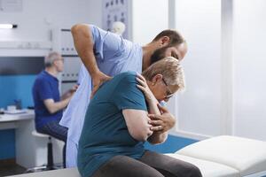 Caucasian senior woman receives checkup from physiotherapist. Patient, recovering from back pain, undergoes spinal pressure examination and engages in rehabilitative exercises with guidance. photo