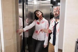 Workers coming out of office building elevator dressed as creepy zombies during Halloween holiday. Colleagues covered in fake scars pretending to be feral cadavers exiting escalator photo