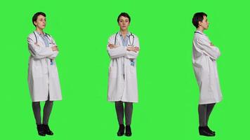 Woman medic posing with arms crossed in a white coat, feeling confident and successful with her medical career and expertise. Doctor having a stethoscope standing against greenscreen. Camera A. photo