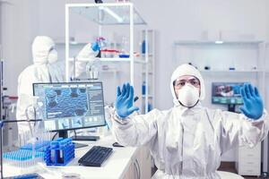 Healthcare engineer in laboratory looking at digital screen holding hands up. Medical scientist using modern technology to cure diseases and develop a cure. photo