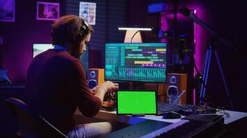 Musician mixing and mastering sounds at home studio with electronic console and soundboard, creating modern tunes. Sound engineer producing audio tracks with greenscreen on tablet. Camera B. photo